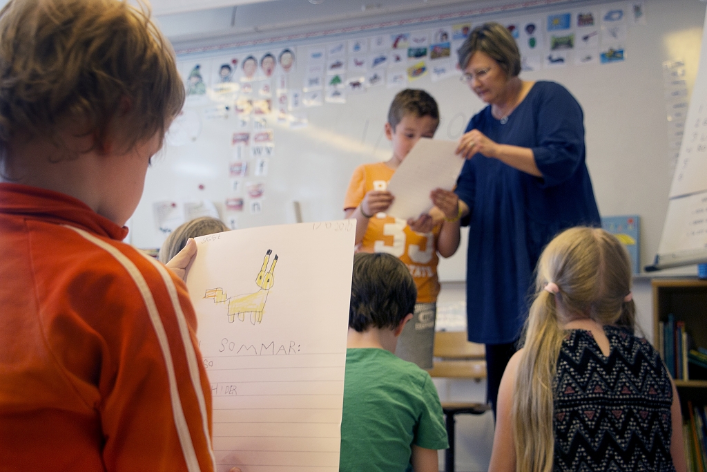 Barn håller i papper i ett klassrum.