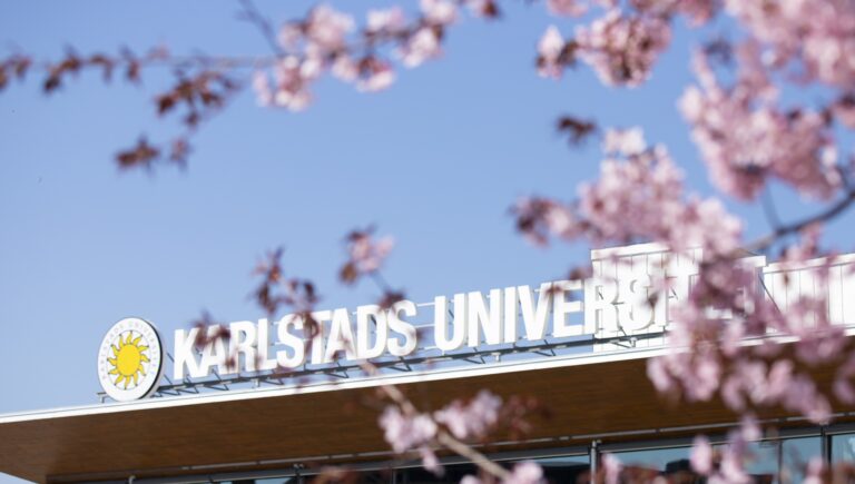 Skylt Karlstads universitet med körsbärsblom i förgrunden.