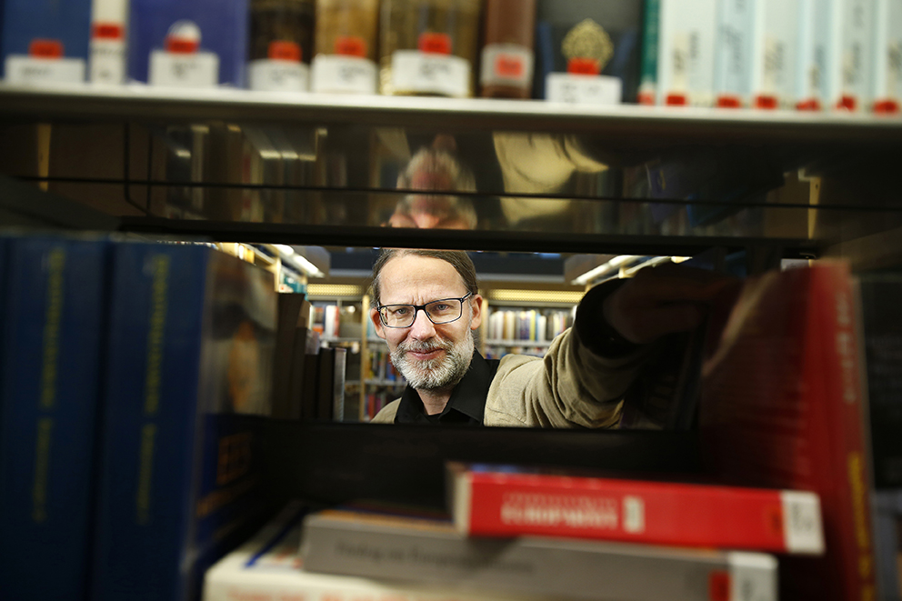Forskare Johan Samuelsson tittar fram genom en bokhylla med fackböcker i ett bibliotek.