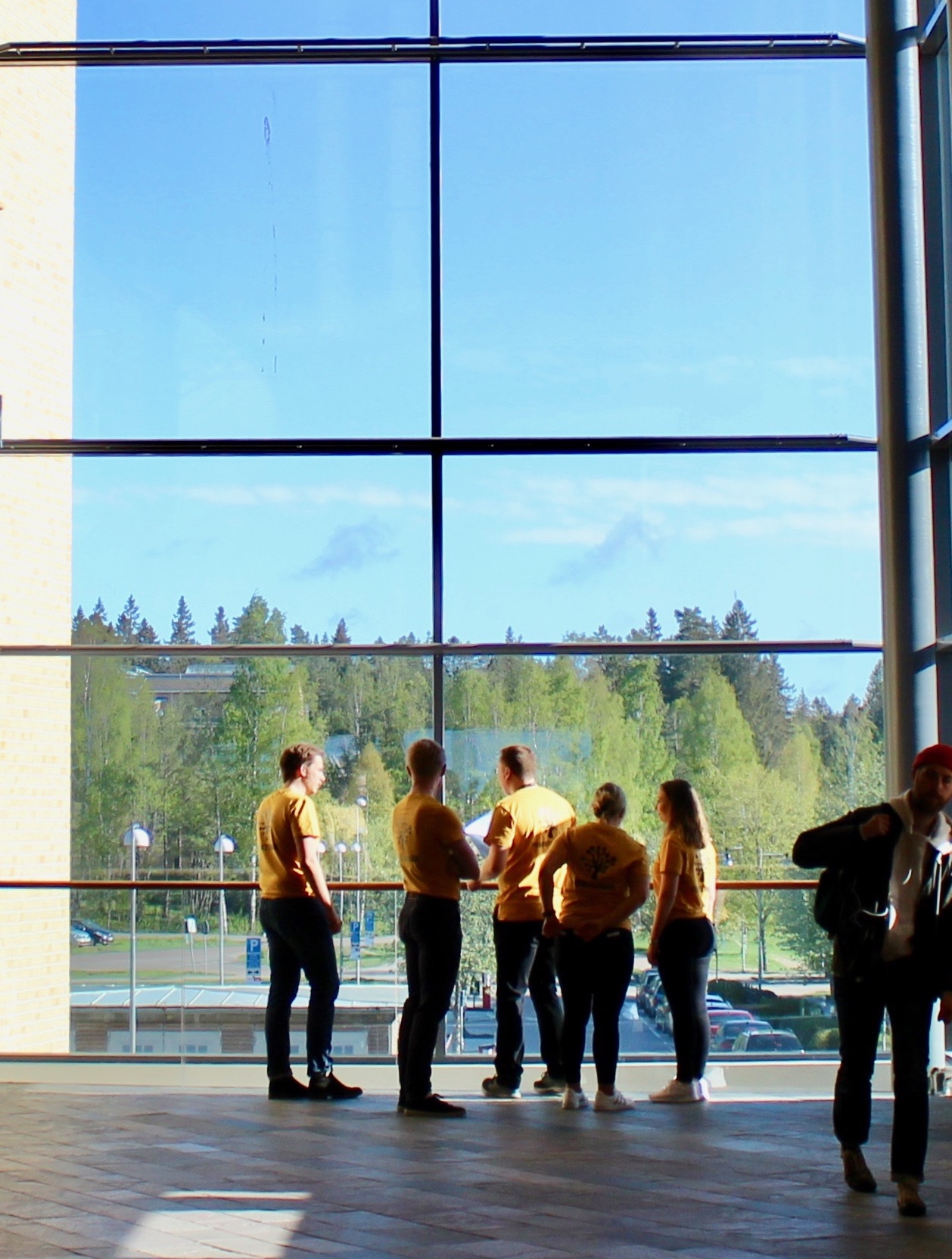 Studenter i orange t-shirt framför ett många meter högt fönster på Karlstads universitet.