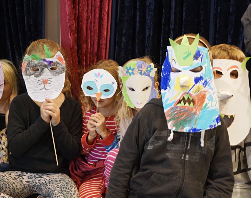 Fem barn står med sina färgglada masker framför ansiktet. 