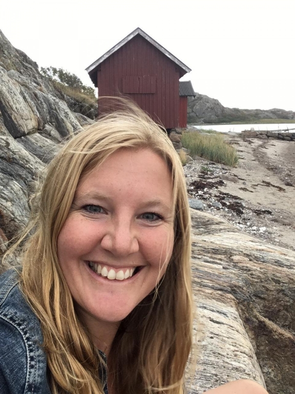 Forskaren Sara Blanck med klippor, vatten och ett röda båtsskjul i bakgrunden.