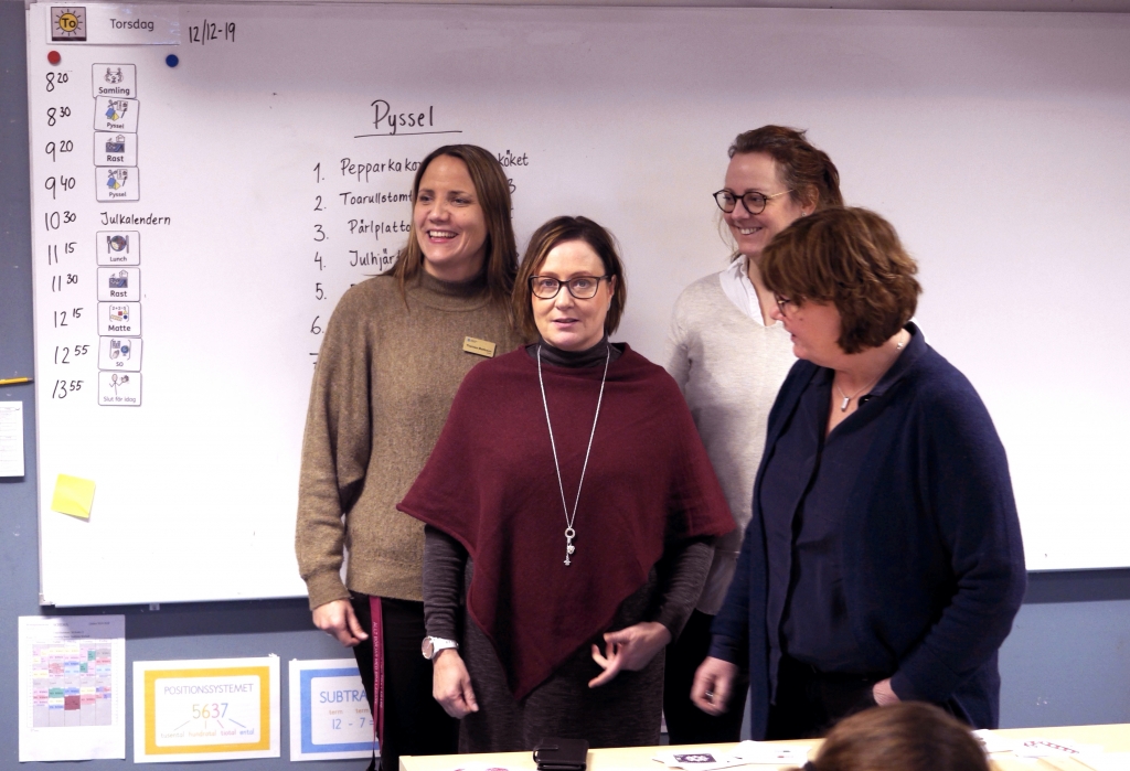 Fyra kvinnor framför tavlan i ett klassrum, en tittar in i kameran och de andra skrattar och tittar åt olika håll.