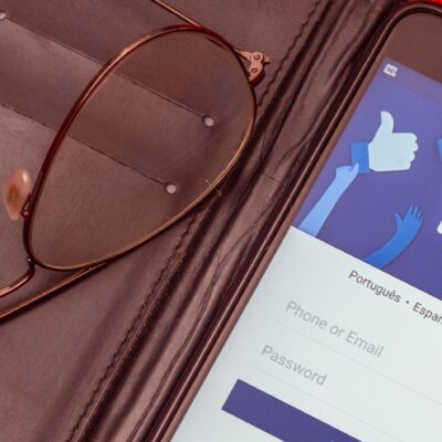 En mobiltelefon med inloggningssidan på facebook i ett brunt fodral med ett par glasögon.