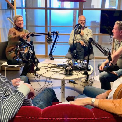 Fyra personer i en ljudstudio framför varsin mikrofon och en tekniker.