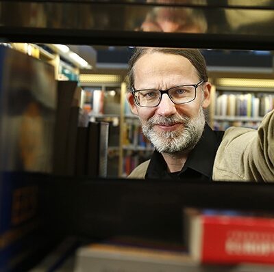 Forskaren Johan Samuelsson tittar fram genom en bokhylla med facklitteratur på ett bibliotek.