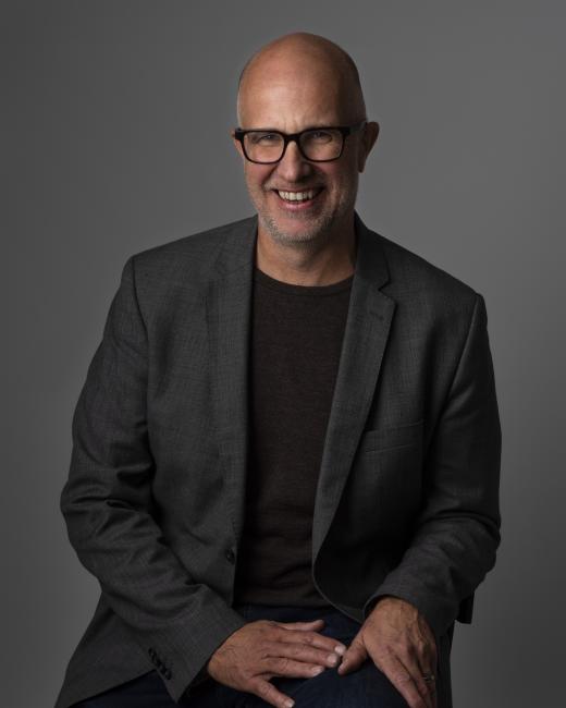 En leende Martin Stolare i glasögon, svart tshirt och kavaj