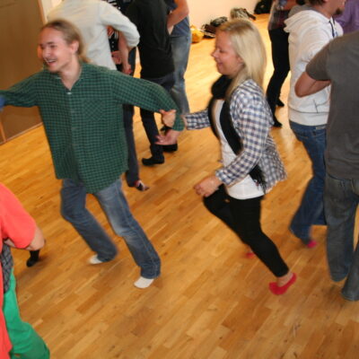 En grupp personer som dansar ringdans i en sal med trägolv.